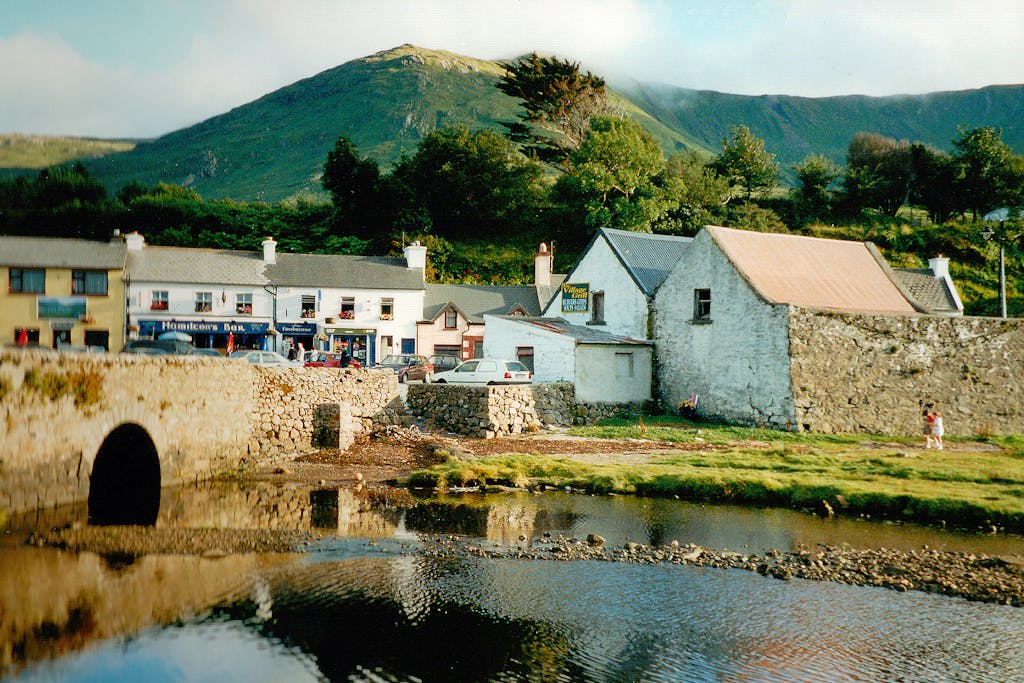 Scenic view of an Irish village with a stone bridge and a mountainous backdrop, captured in daylight.